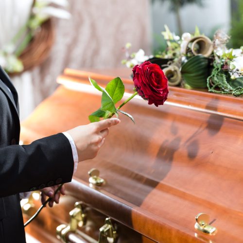 Mourning woman on funeral with red rose standing at casket or coffin