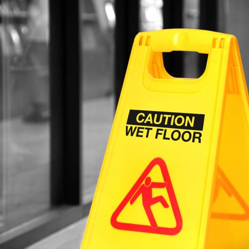 Bright yellow caution sign of wet floor in a hallway. Conceptual image with isolated color over black and white background